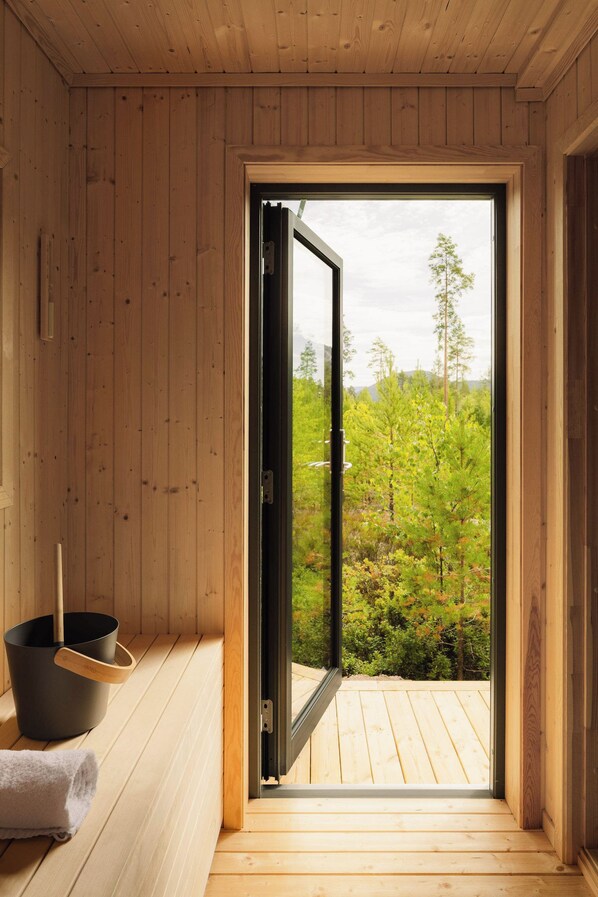 A wooden sauna room with a large sliding door leading to an outdoor area with greenery.