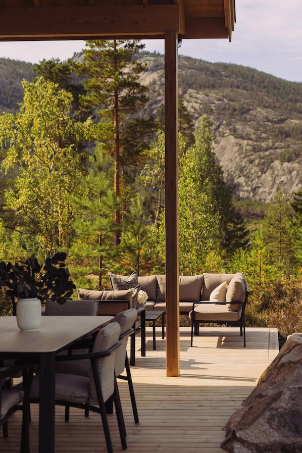 An outdoor deck with a wooden table and chairs, a sofa, and a view of a mountainous landscape.