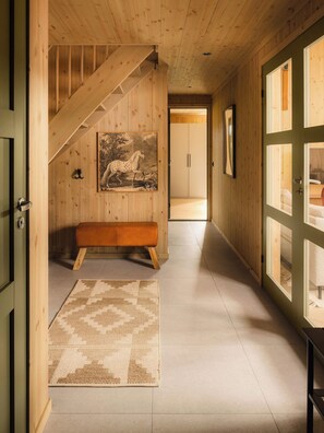 A wooden interior hallway with a bench, a staircase, and a door leading to another room.
