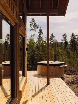 A wooden deck with a hot tub and a glass door leading to a room.