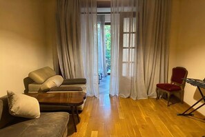A living room with a sofa, a red chair, a wooden coffee table, and a keyboard. - 2-Bedroom Apartment in Tranquil Tbilisi Perfect for Relaxing Stays (T'bilisi)
