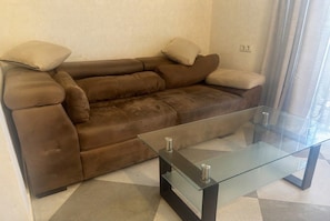 Un canapé en cuir marron avec des coussins, une table basse en verre et un sol carrelé.
