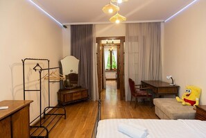 A hotel room with a bed, a desk, a chair, a wardrobe, and a hanging clothes rack. - 2-Bedroom Apartment in Tranquil Tbilisi Perfect for Relaxing Stays (T'bilisi)