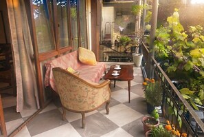 A balcony with a checkered floor, a floral armchair, a small table with a cup, and potted plants. - 2-Bedroom Apartment in Tranquil Tbilisi Perfect for Relaxing Stays (T'bilisi)
