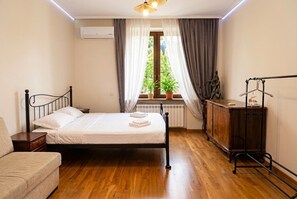 Une chambre à coucher comprenant un lit, une table de chevet, une commode, un radiateur et une fenêtre avec des rideaux.