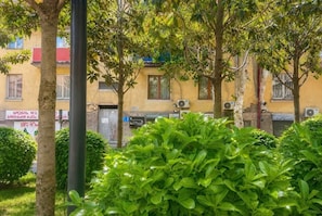 Un edifici amb diverses finestres, algunes amb aparells d'aire condicionat, envoltat de arbustos i arbres de fullatge abundant.