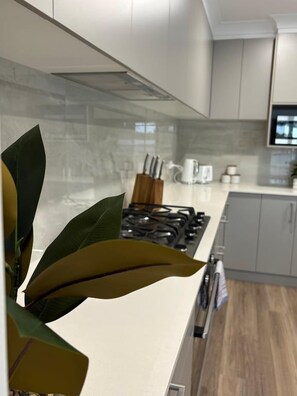 Een moderne keuken met een gasfornuis, witte kastjes en een aanrecht met keukengerei.
