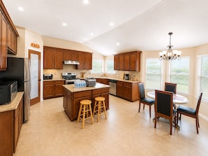 A spacious kitchen with wooden cabinets, a central island with stools, a dining area with chairs, and a chandelier. - Spacious 4 bedrooms with 5 beds house very close to Food hood (Killeen)