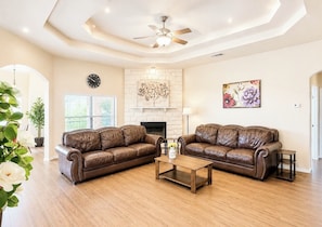 A spacious living room with two leather sofas, a wooden coffee table, a fireplace, and a ceiling fan. - Spacious 4 bedrooms with 5 beds house very close to Food hood (Killeen)