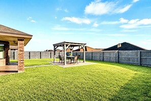A backyard with a covered patio area, a wooden fence, and a well-maintained lawn. - Spacious 4 bedrooms with 5 beds house very close to Food hood (Killeen)