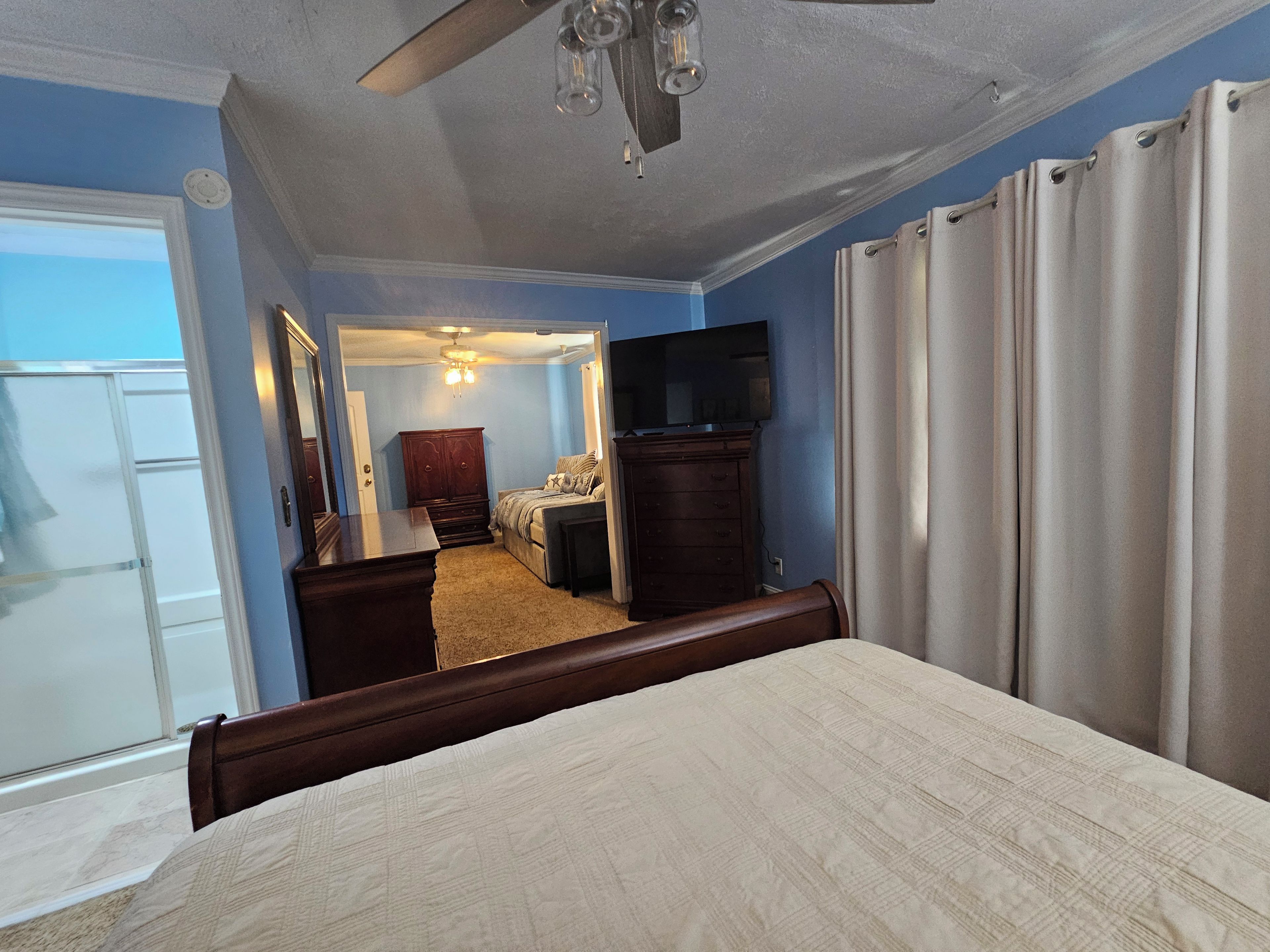 Un dormitorio con cama, cómoda, televisor y ventilador de techo.