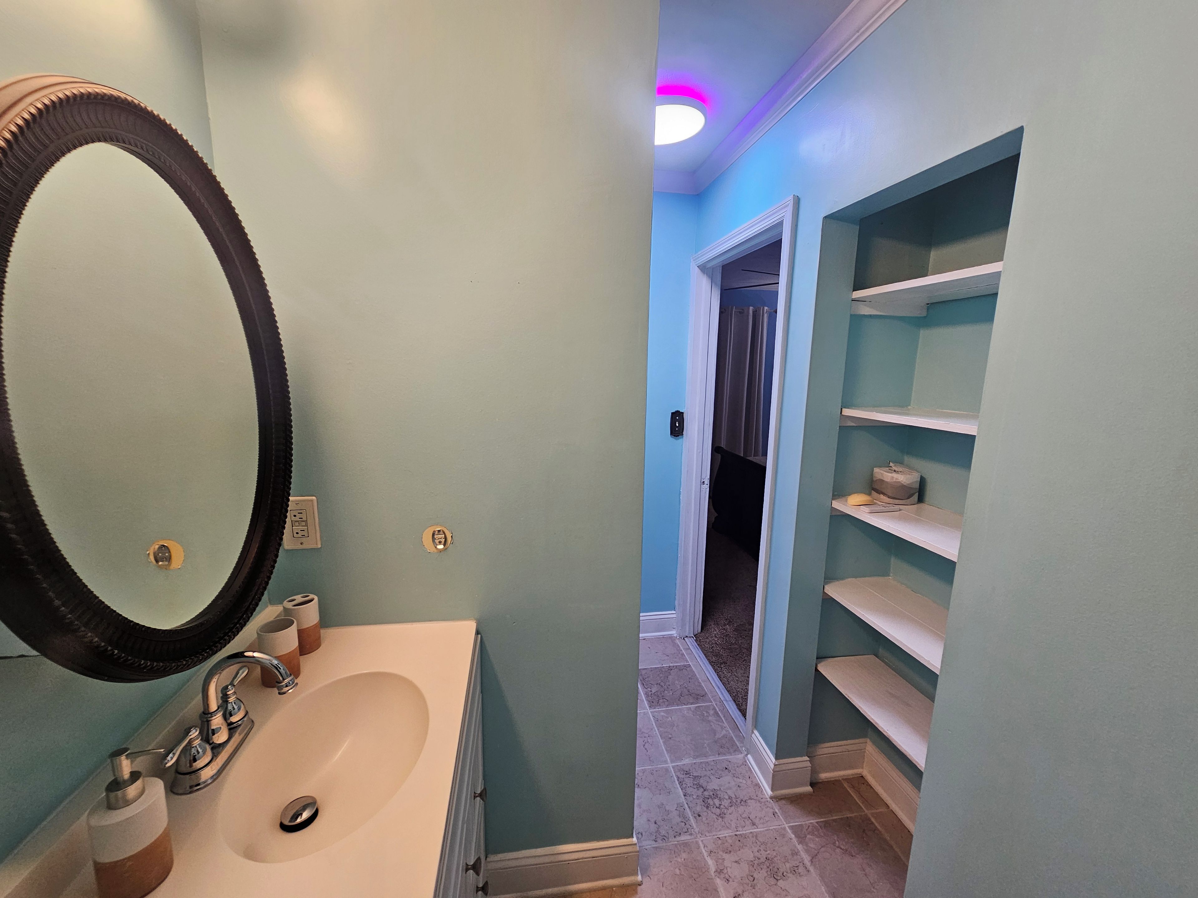 A bathroom with a sink, mirror, and shelves.