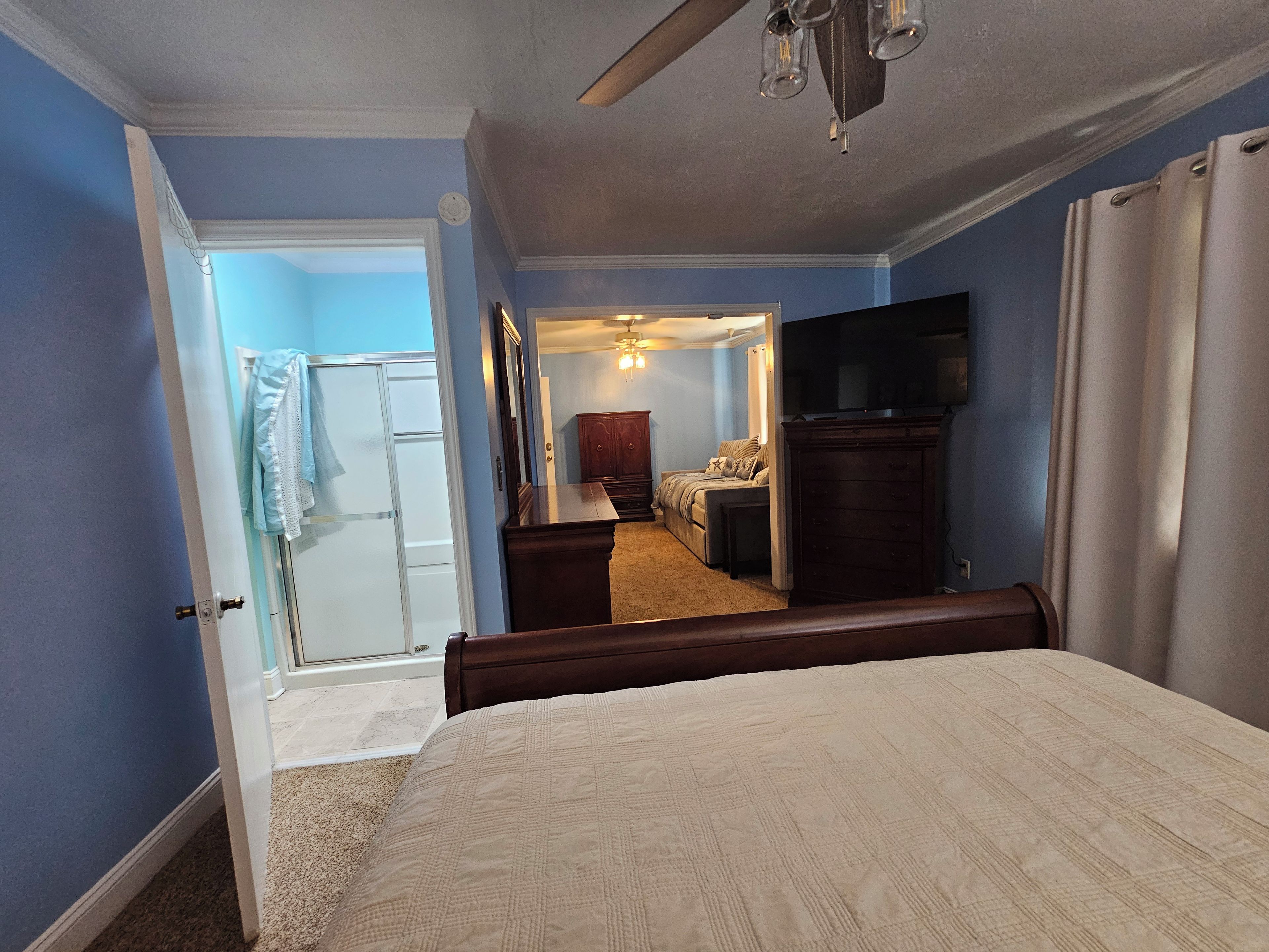 Une chambre à coucher comprenant un lit, une commode, un téléviseur et une porte donnant sur une salle de bain.