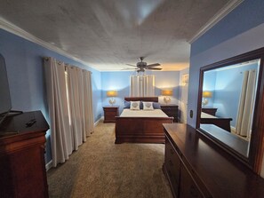 Ein Schlafzimmer mit einem Bett, zwei Nachttischen, einem Deckenventilator, einem großen Spiegel und einer Kommode.