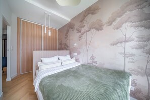 Un dormitori amb llit, un armari i una paret amb un dibuix d'un arbre.