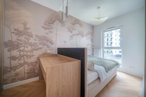 A bedroom with a bed, a wooden desk, a wall mural, a window with a view of buildings, and a ceiling light fixture. -  Kierbedzia Blue Sapphire Residence (Warszawa)