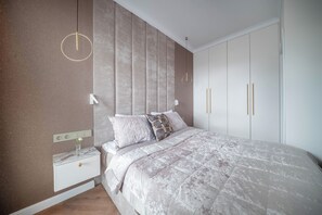 Een slaapkamer met een bed, nachtkastje, wandlamp, kledingkast en een stopcontact.