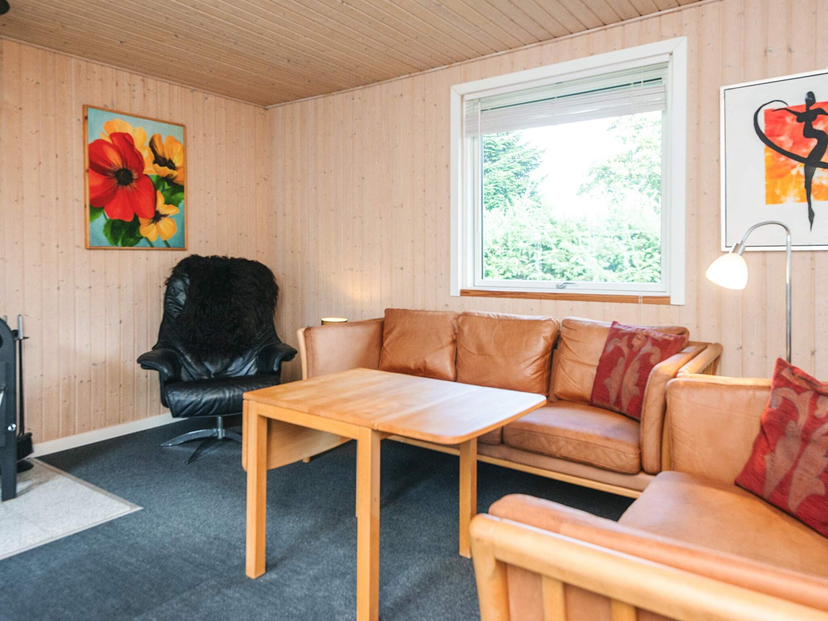 Ein Zimmer mit Holzboden, einem Fenster mit Blick auf Grünflächen, einem schwarzen Ledersessel, einem braunen Ledersofa und einem Holztisch.