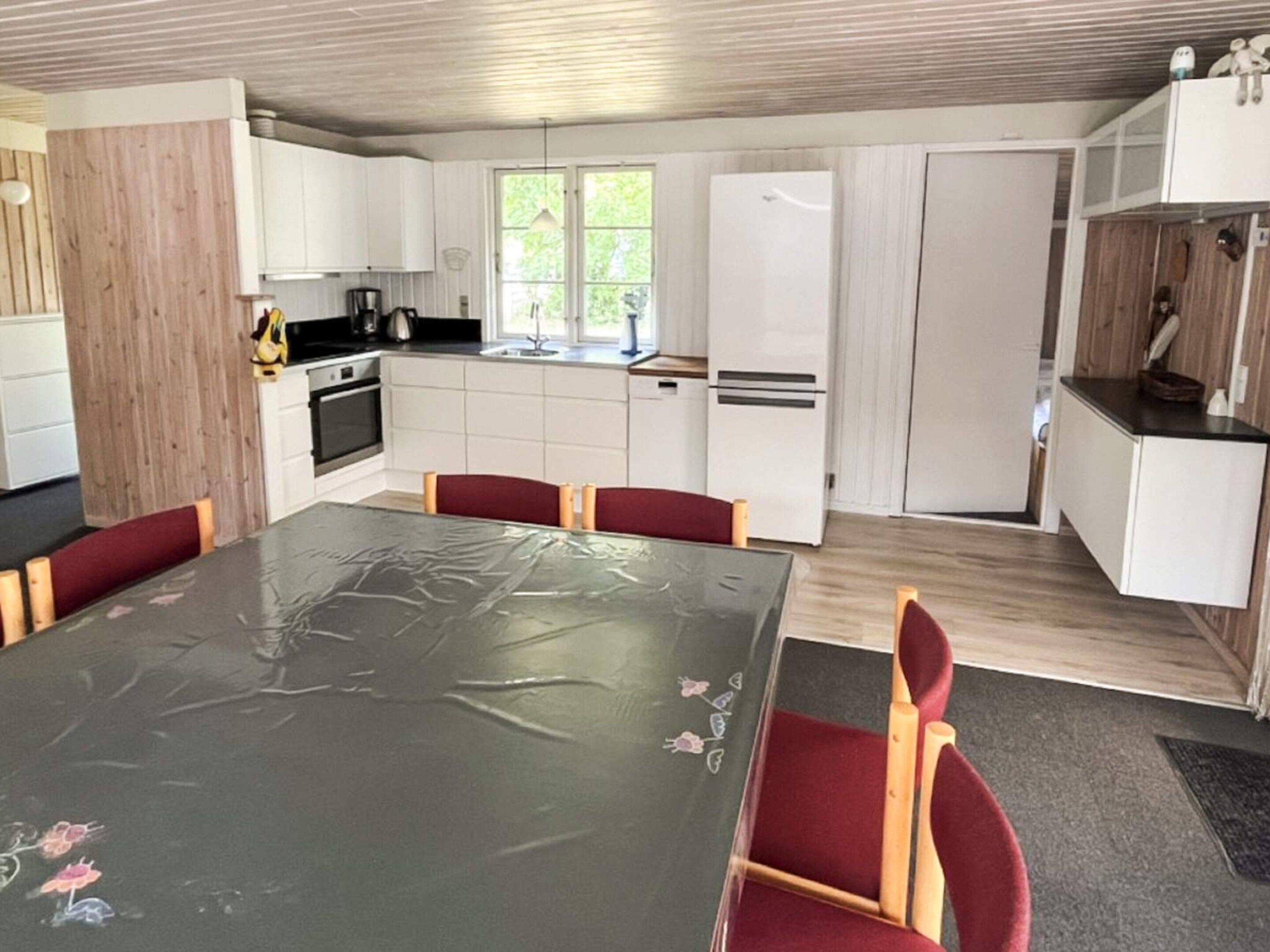 A modern kitchen with white cabinets, a dining table with chairs, and a refrigerator.