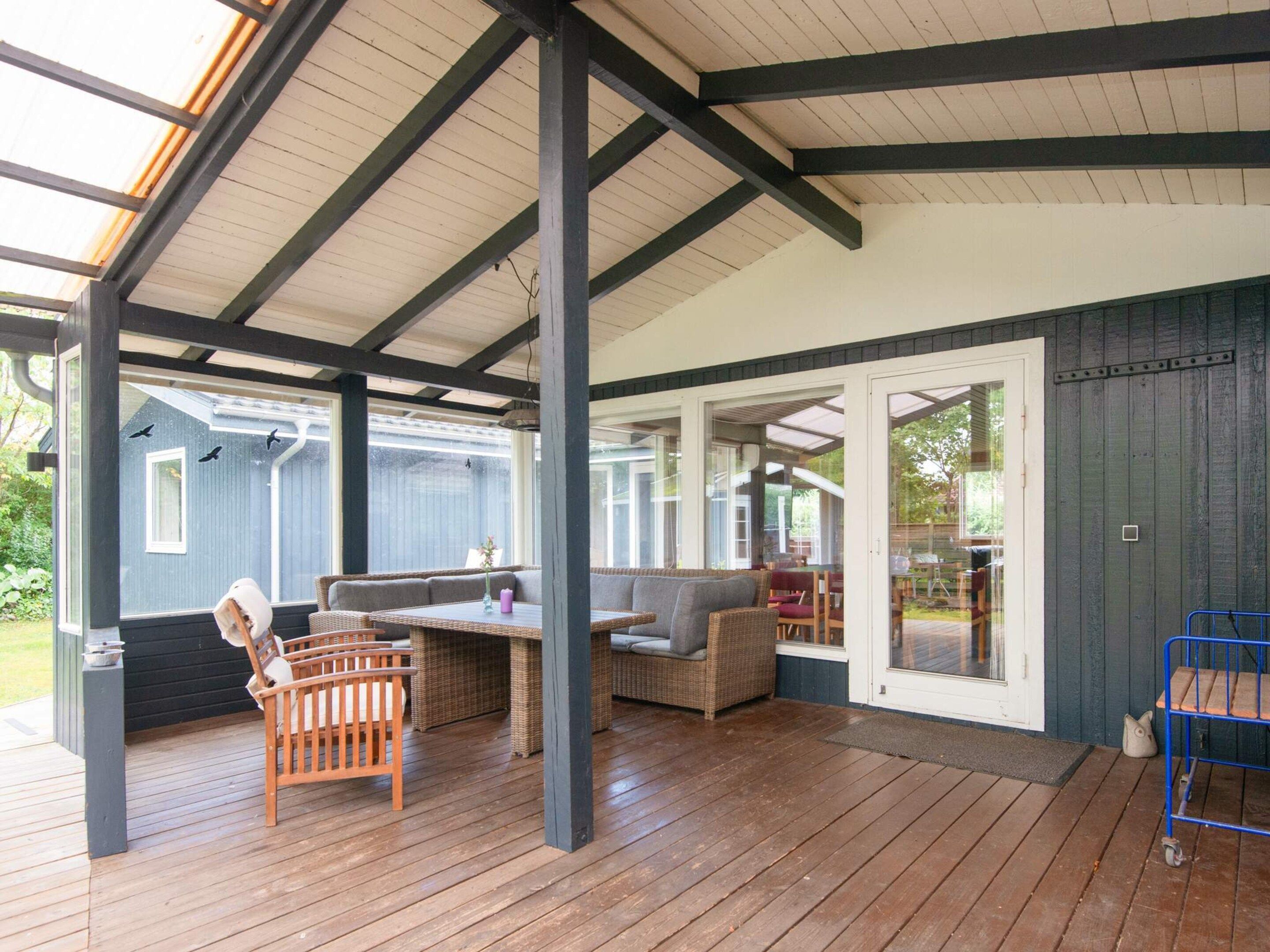 A covered outdoor seating area with wooden flooring, built-in benches, and a glass door leading to an adjacent room.