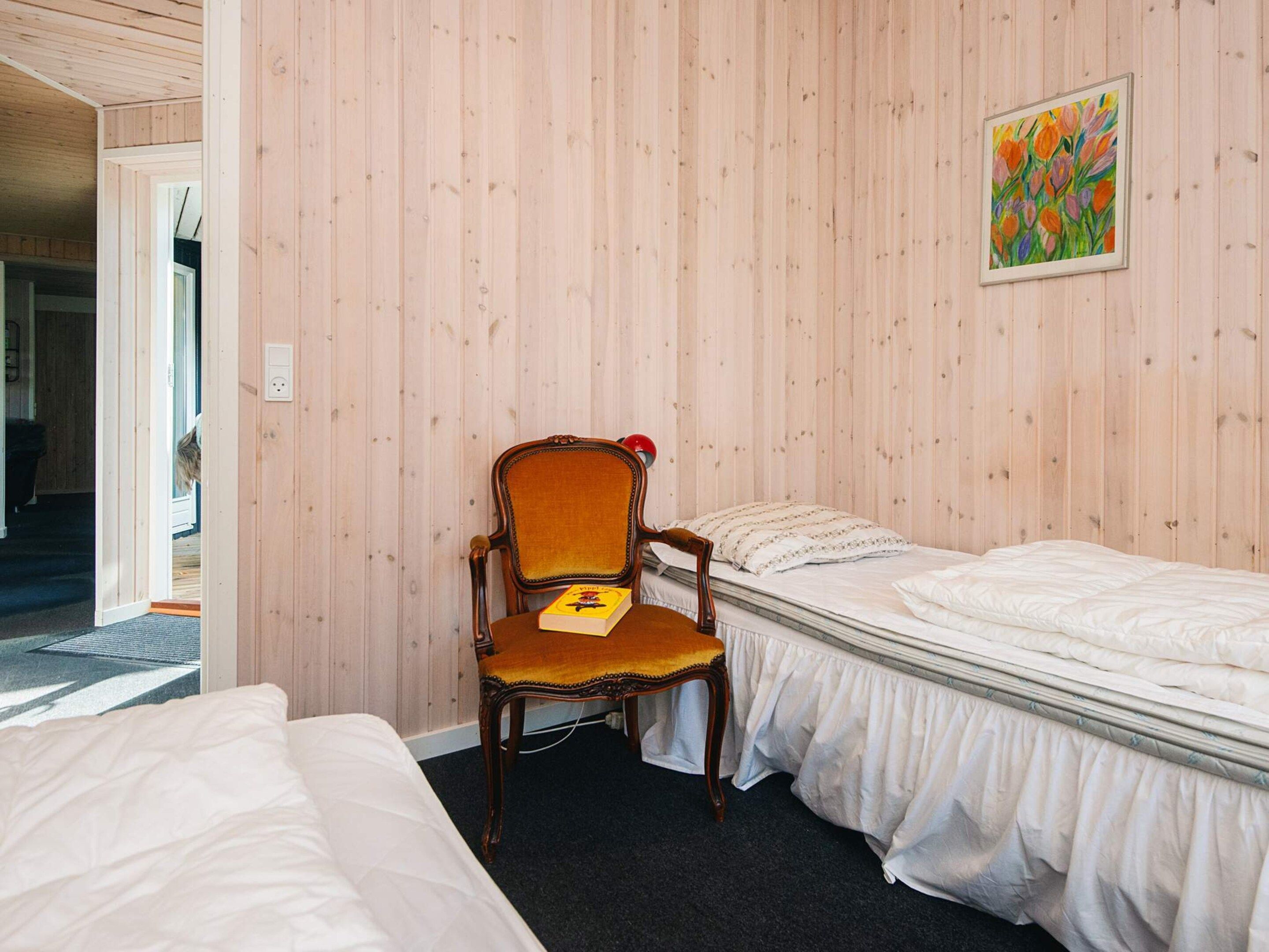 A room with two beds, a wooden chair, and a painting on the wall.
