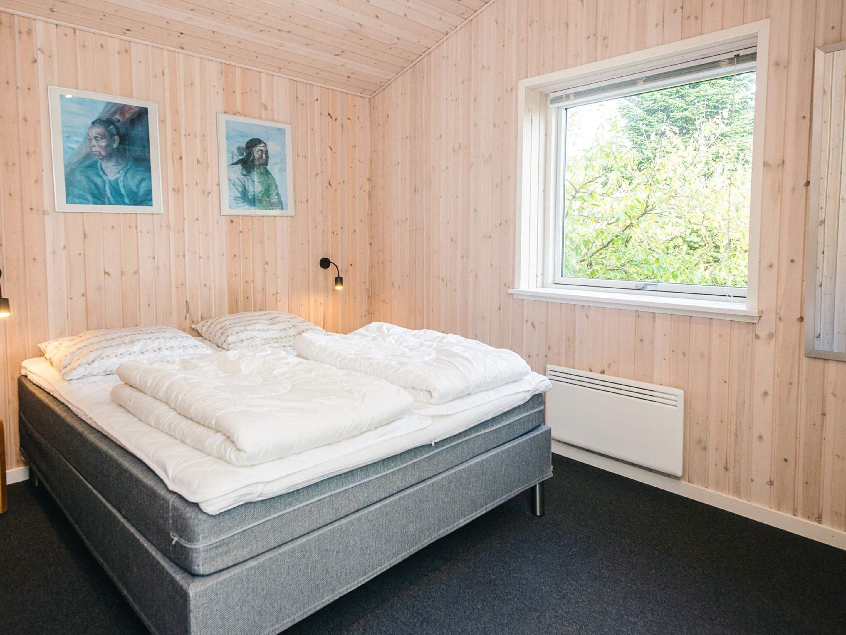 Un dormitorio con una cama, dos lámparas de pared, un ventanal y dos cuadros enmarcados.