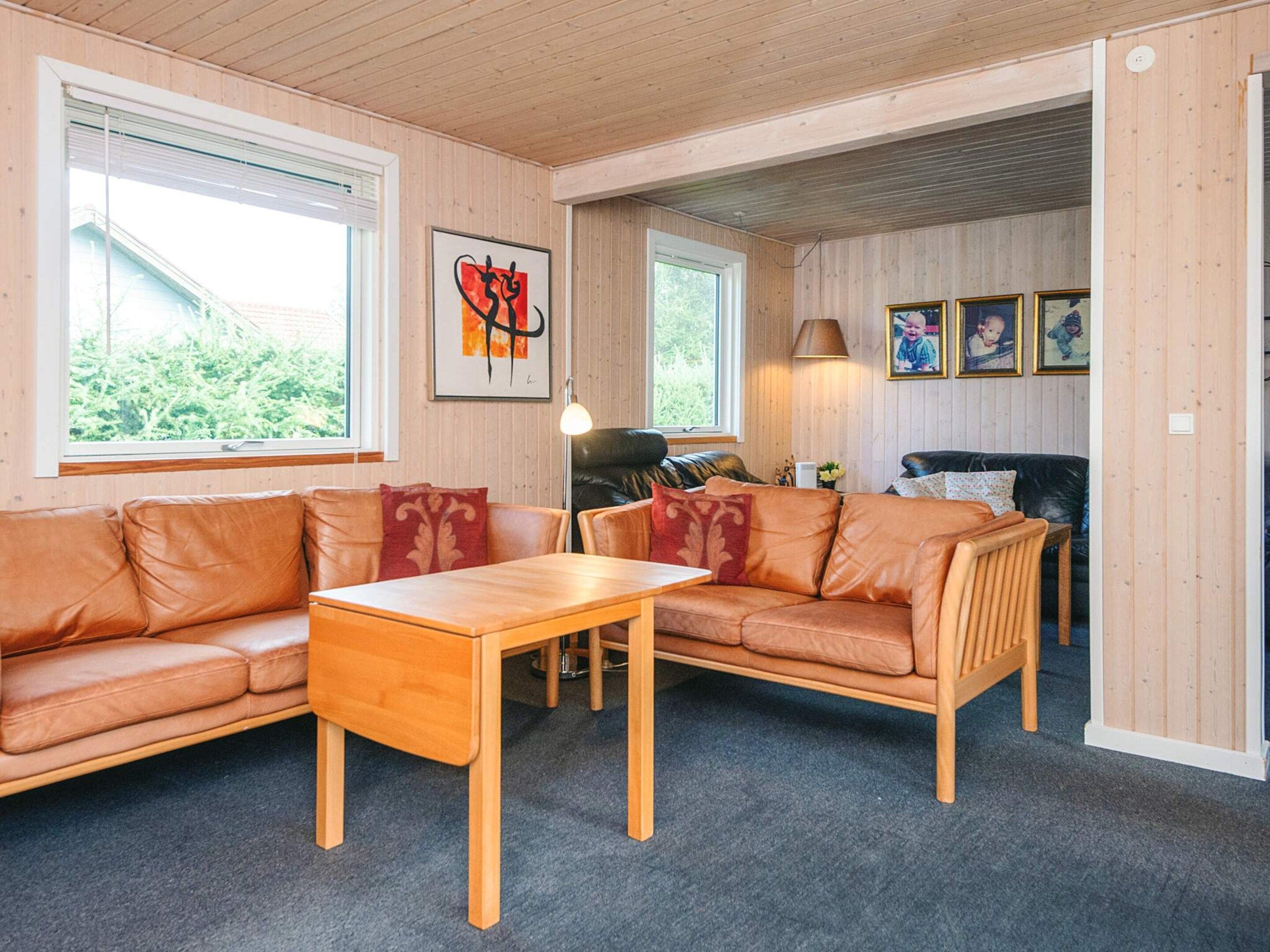 A cozy living room with a wooden ceiling, two leather sofas, a wooden coffee table, and a large window.