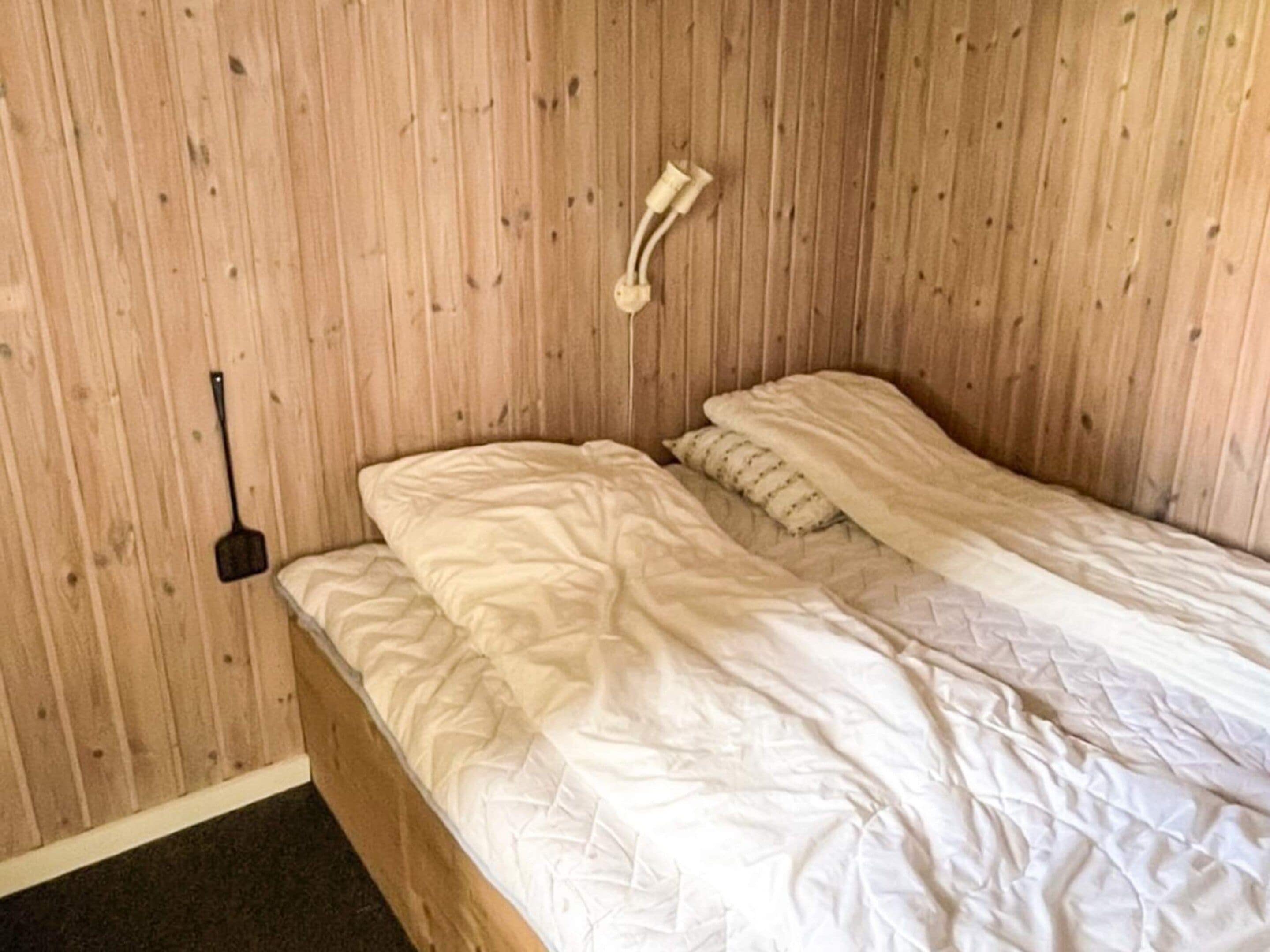 A single bed with a white duvet and a headboard against a wooden wall.