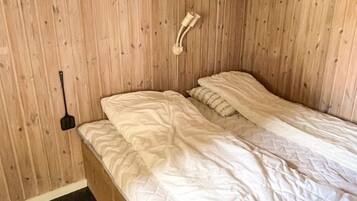 A single bed with a white duvet and a headboard against a wooden wall.