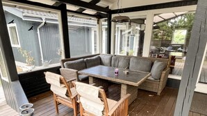 Eine Terrasse im Freien mit einem Holztisch und Stühlen, einer gepolsterten Bank und einer Pergola.