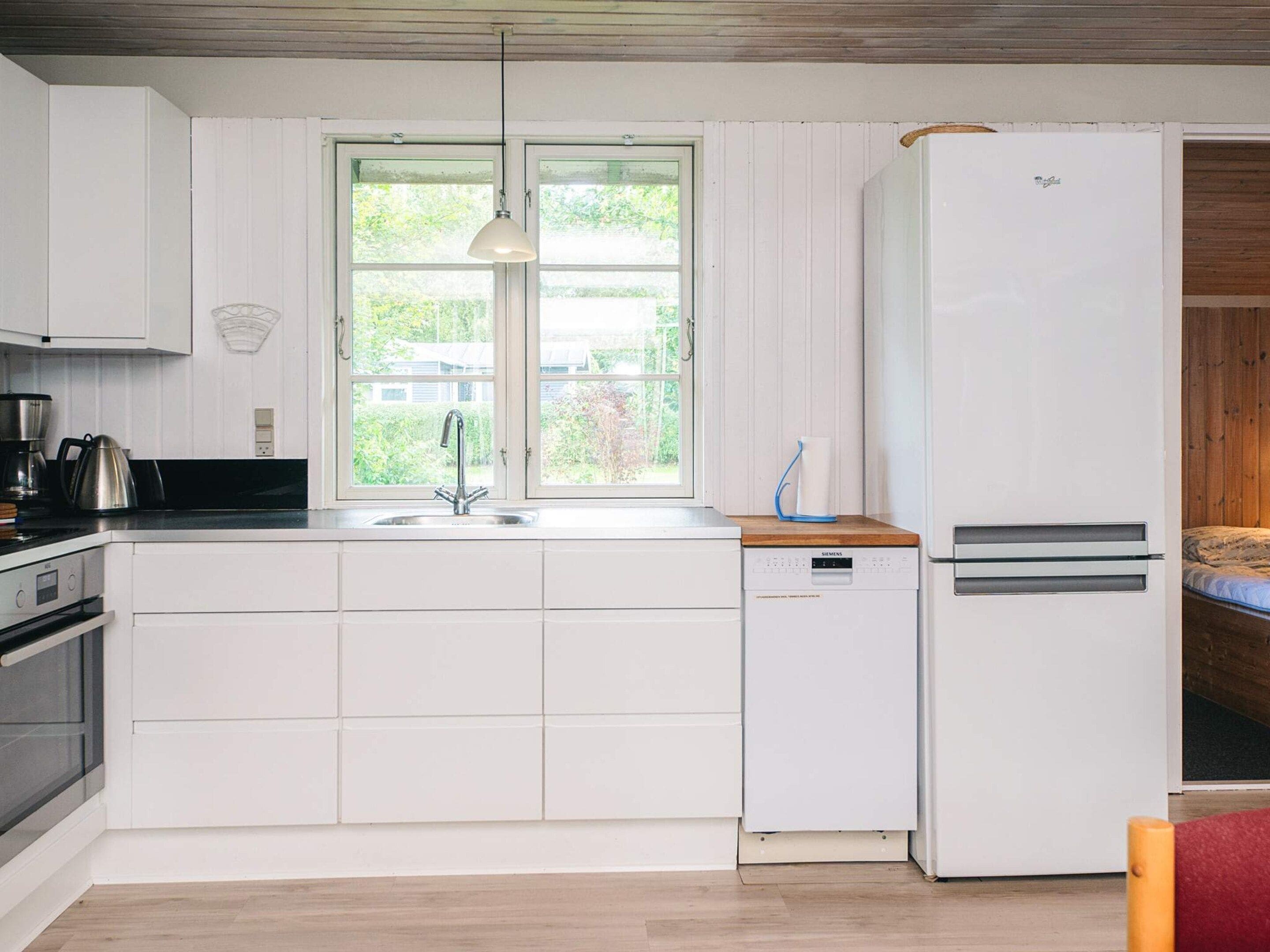 Cocina compacta con armarios blancos, lavavajillas integrado y refrigerador.