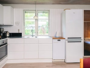 Une cuisine compacte avec des meubles blancs, un lave-vaisselle encastré et un réfrigérateur.
