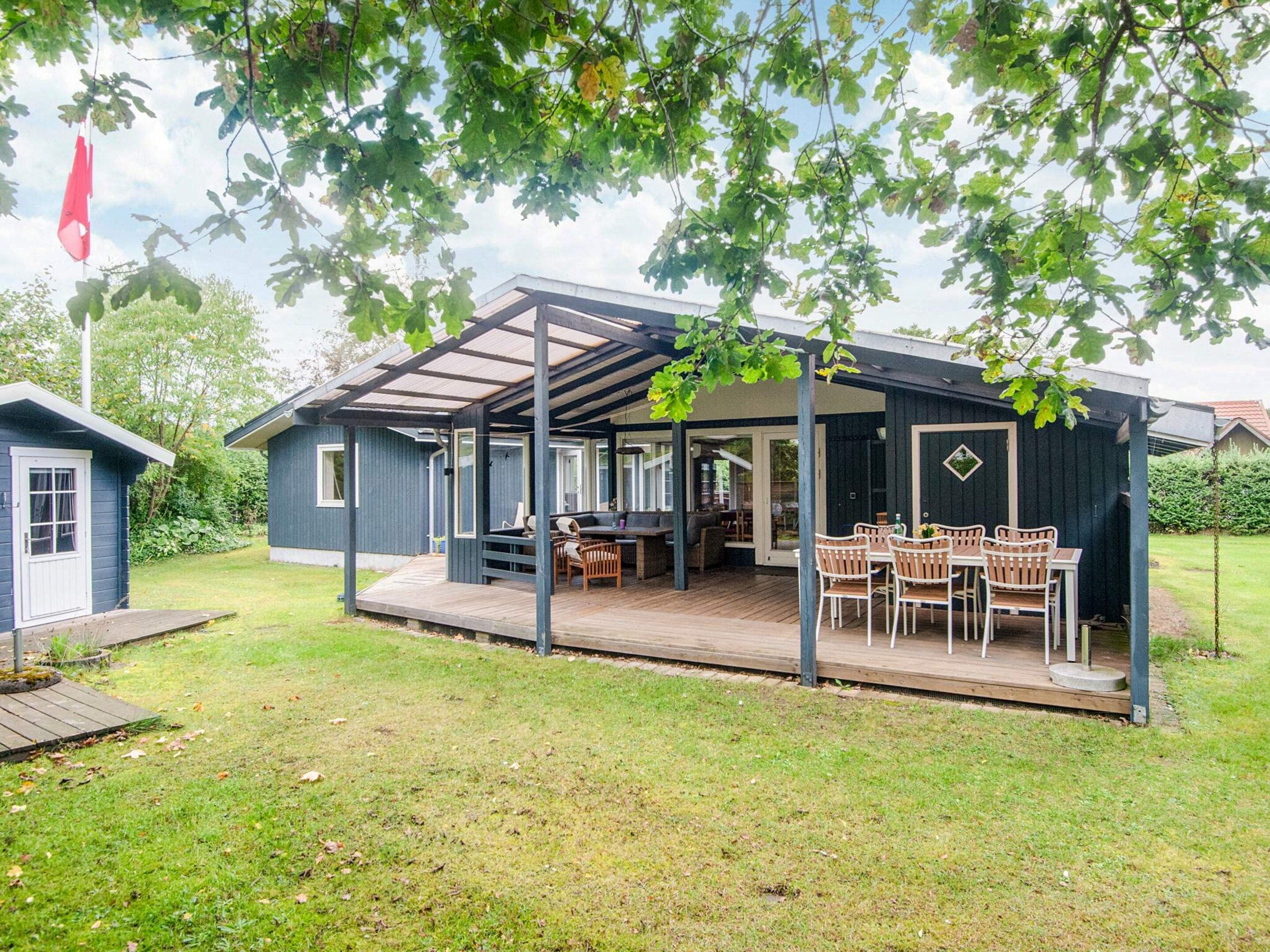 Een overdekt buitengebied met een eettafel en stoelen, een barbecue en een kleine schuur.