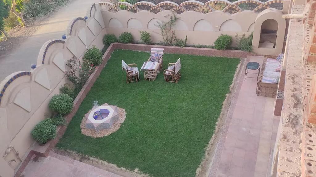 Une cour avec une petite pelouse, une table et des chaises, et une fontaine décorative.
