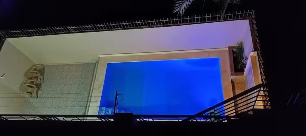 Une pièce dotée d’une grande fenêtre aux reflets bleutés, d’un escalier et d’une petite plante.