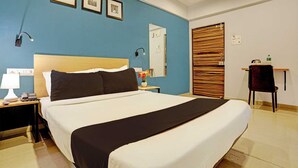 A hotel room with a large bed, a nightstand with a lamp, a desk with a chair, and a wooden door. - Classic Bhumi Stay inn (Bhiwandi)