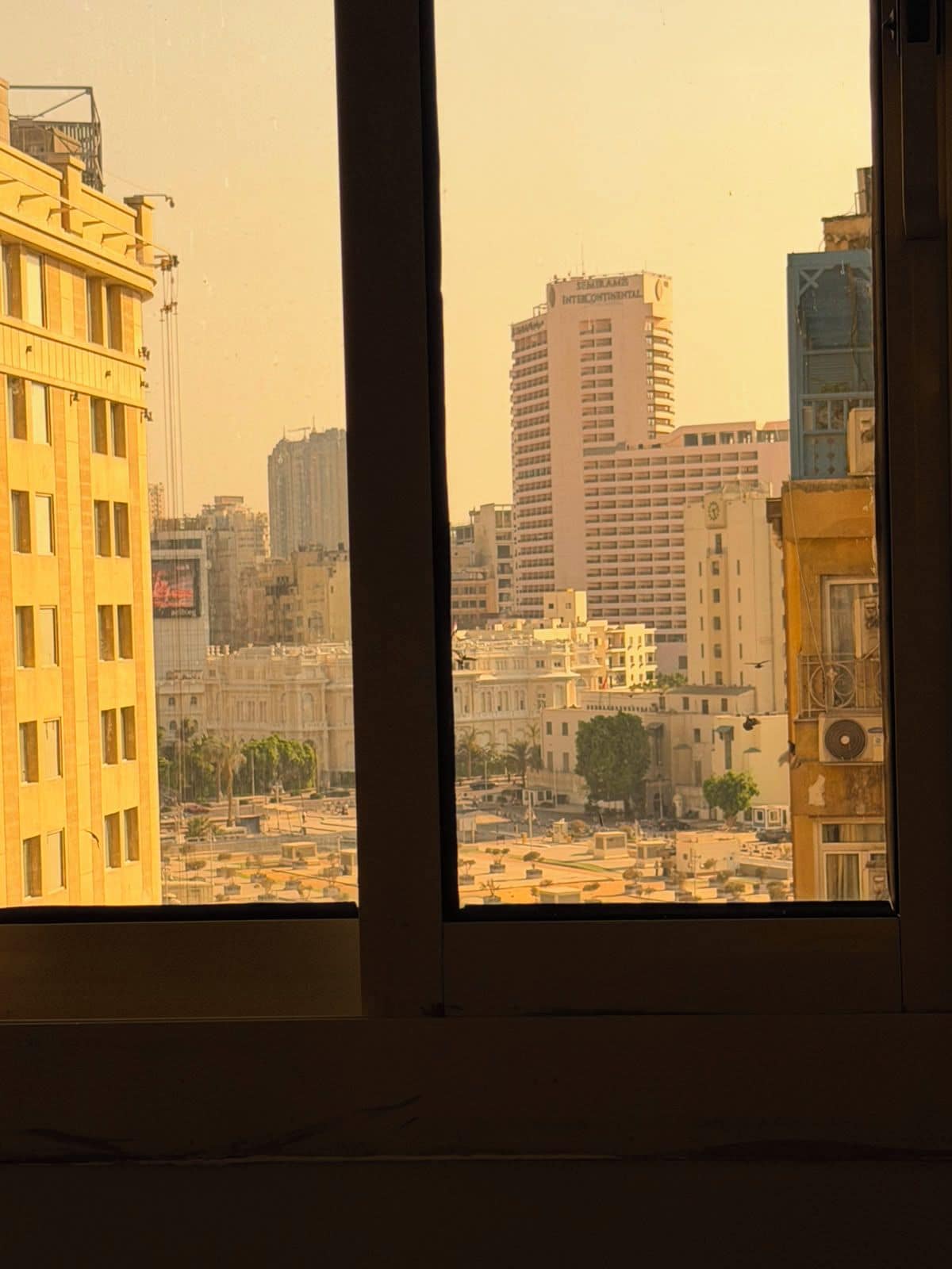 Vista per una finestra d'un paisatge urbà amb diversos edificis, incloent un gratacels i diverses construccions de mitjana alçada.