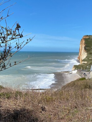 A coastal landscape with a cliff, beach, and a road leading to a building.
