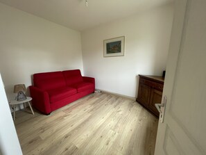 A room with a red sofa, a small table with a lamp, a cabinet, and a framed picture on the wall.