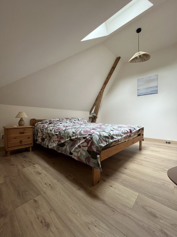 A bedroom with a sloped ceiling, a bed with a floral bedspread, a nightstand with a lamp, and a painting on the wall.