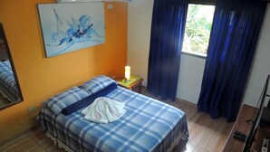 Une pièce comprenant un lit, une table de chevet, une lampe, une fenêtre avec des rideaux et un tableau accroché au mur.