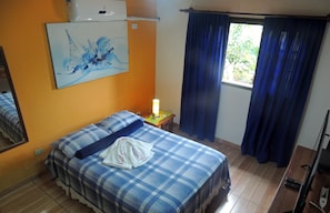 A room with a bed, a nightstand, a lamp, a window with curtains, and a painting on the wall.