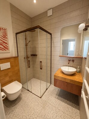Ein modernes Badezimmer mit einer Duschkabine aus Glas, einer weißen Toilette und einem Waschbecken mit Holzablage.