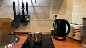 A kitchen with a black induction cooktop, a kettle, a toaster, and hanging utensils.