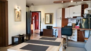 A modern living room with a dining table, a sofa, and a kitchen area with cabinets and a microwave.