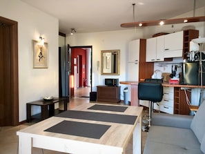 A modern living room with a dining table, a sofa, and a kitchen area with cabinets and a microwave.