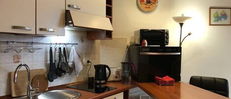 A compact kitchen with a sink, stove, and microwave. There is a dining table with chairs.