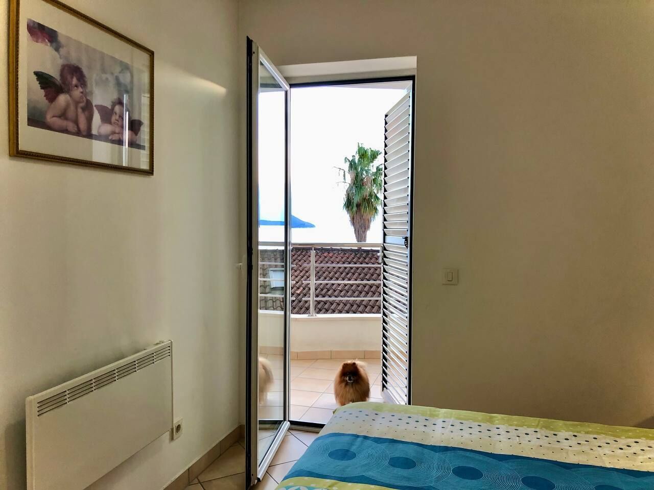 Una camera da letto con un letto, un termosifone, una porta scorrevole in vetro che dà su un balcone e un quadro appeso al muro.