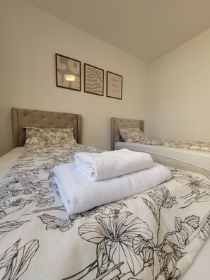 A hotel room with two beds, each with a floral-patterned bedspread and matching pillows. There are three framed pictures on the wall above the beds.