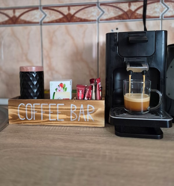 A coffee bar setup with a coffee machine, a glass mug, and coffee pods on a wooden board labeled 'COFFEE BAR'.